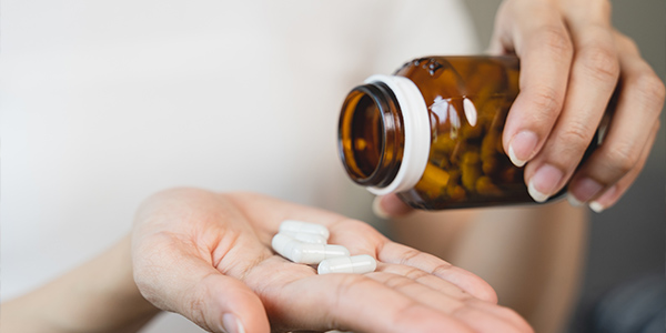 a woman tilting a bottle of multivitamins into her palm