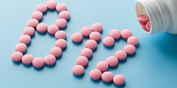 Pink round vitamins B12 shaped pills on a blue background spilled from a white can